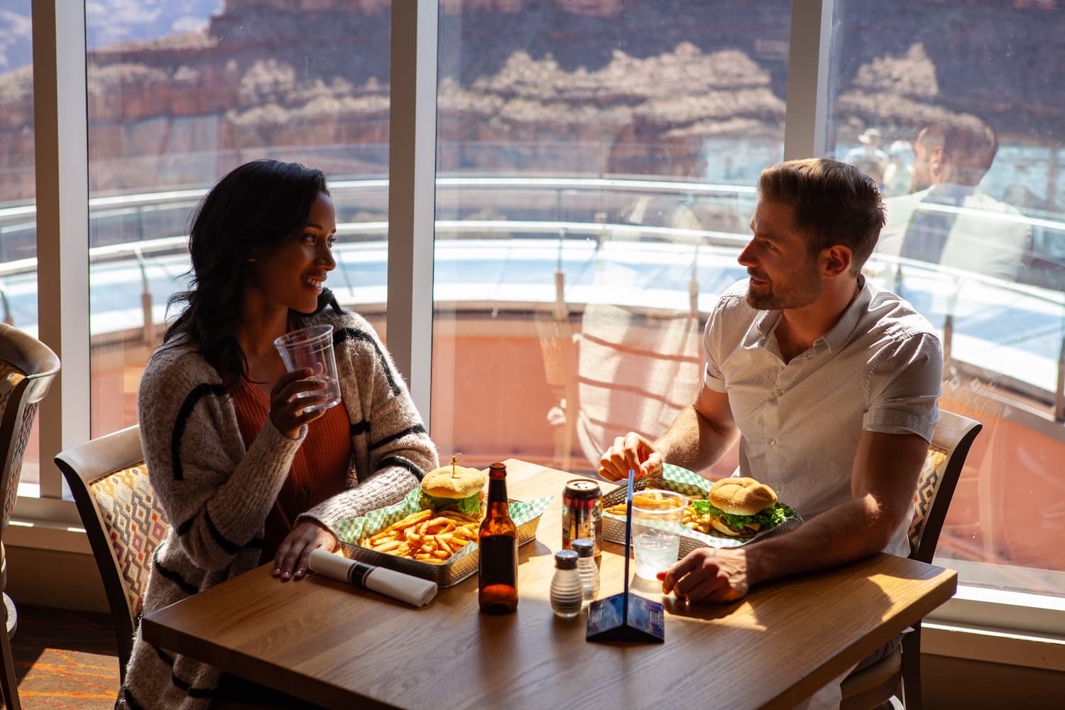 A couple eating burgers and fries at a restaurant with large scenic windows.