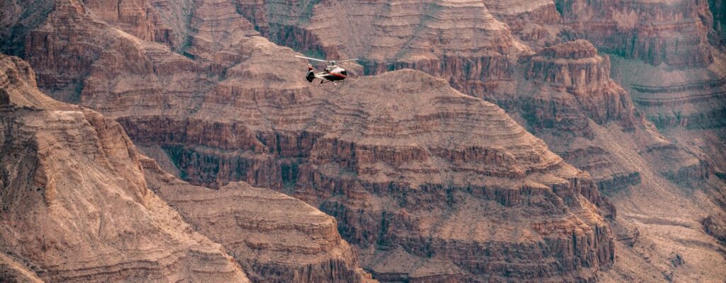A small helicopter flies against the backdrop of the Grand Canyon's layered rock formations.