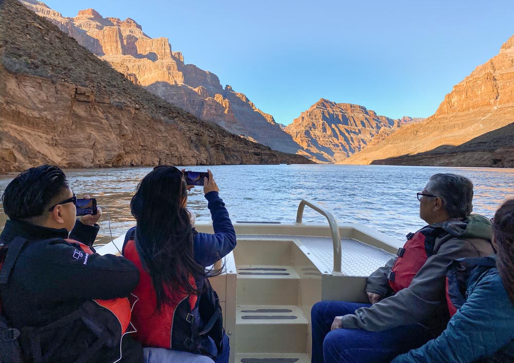 People in life vests ride in a boat on a river, surrounded by steep canyon walls.