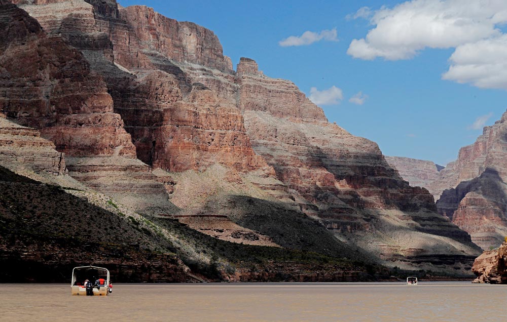 Two boats float on a calm river surrounded by the towering, layered walls of the Grand Canyon.