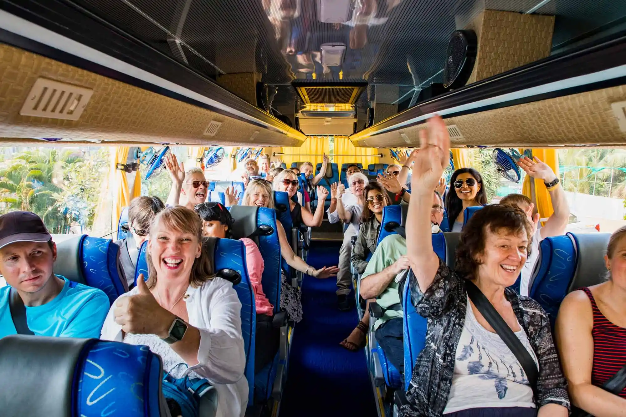 Smiling tourists wave inside a bus.